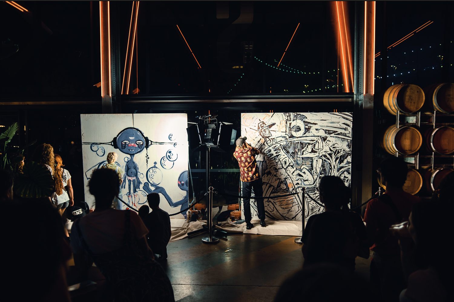 Two finished black-and-white canvases flank an MC on the mic as the crowd looks on